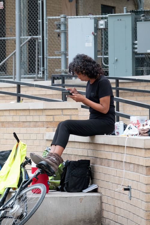 Free Woman sits on a ledge in Austin, Texas, checking her phone near a parked bicycle. Stock Photo