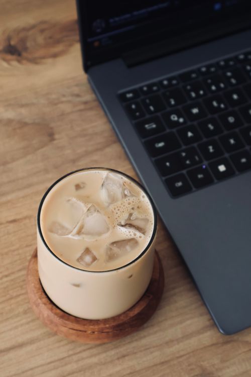 Free Top view of iced coffee in a glass on a wooden desk next to a laptop, ideal for work and relaxation themes. Stock Photo