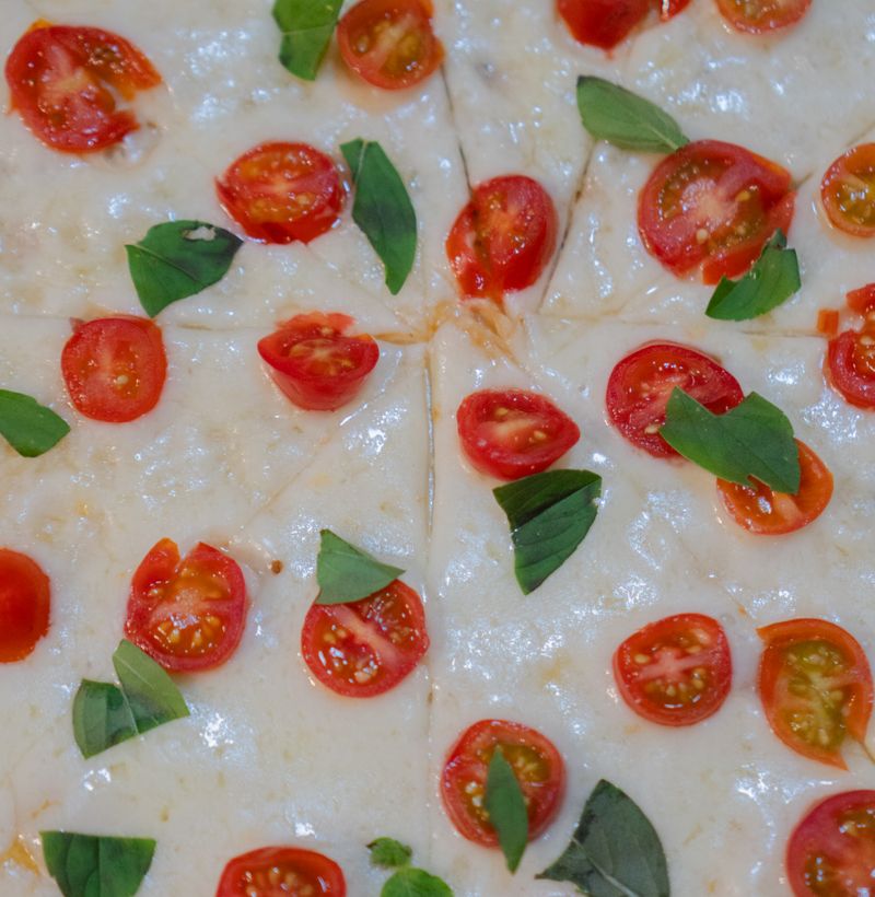 Top view of a Margherita pizza topped with cherry tomatoes and fresh basil leaves.