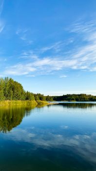 Calm lake scene with reflections of trees under a clear blue sky, perfect for nature themes.