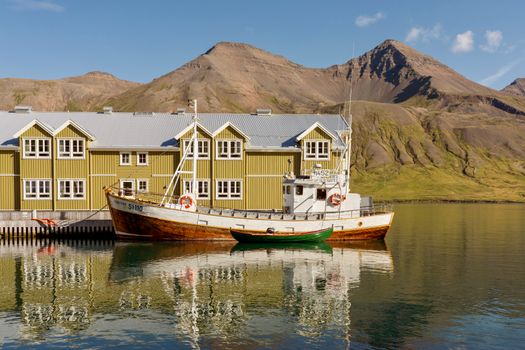 Idyllic Icelandic harbor scene featuring a historic wooden fishing boat and mountains.