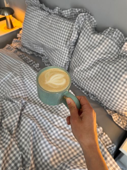 Free A cozy morning scene with a latte in a blue mug on checkered bedding. Stock Photo