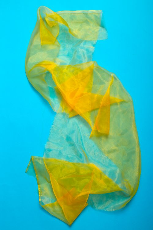 Free Bright sheer yellow fabric on a vivid blue background creates a striking visual contrast. Stock Photo