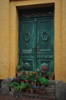 Rustic green door surrounded by colorful potted flowers on steps in Ribe, Denmark.