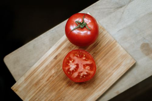 Free Top view of whole and sliced red tomatoes on a wooden cutting board, showcasing freshness. Stock Photo