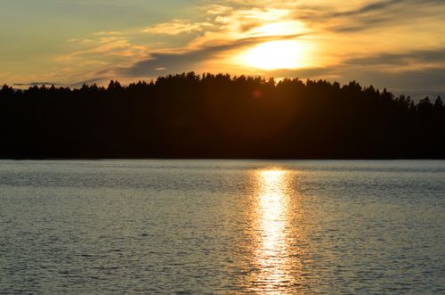 Free Sunset casting warm reflections over a tranquil lake and forest silhouette. Stock Photo