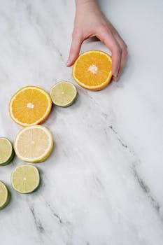 A flat lay of sliced citrus fruits on a marble surface with a hand reaching in.