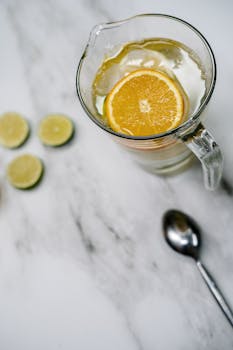 A pitcher of citrus-infused water with orange slices on a marble surface, ideal for a refreshing drink.