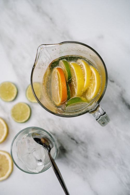 Free Overhead view of a citrus-infused drink with lemon, lime, and orange slices in a glass jug on a marble surface. Stock Photo