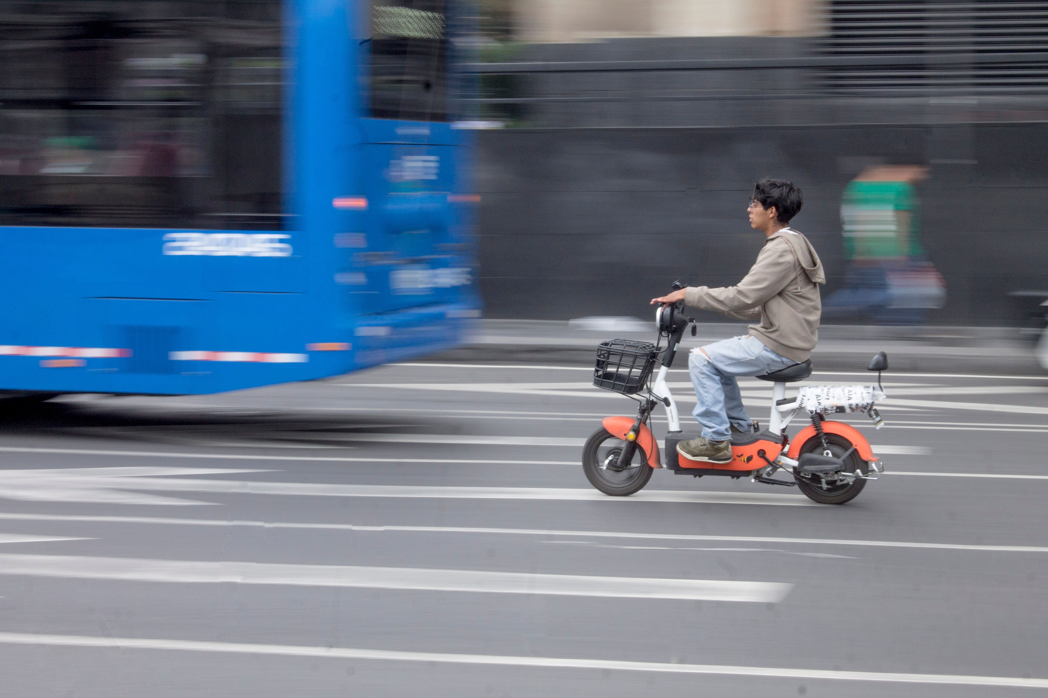 Man riding an electric scooter on a city street with blurred passing traffic.