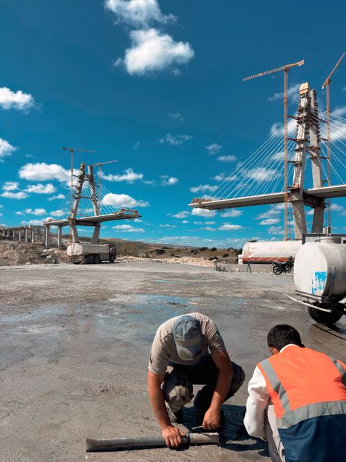 Free Two workers at a bridge construction site with cranes under a bright blue sky. Stock Photo