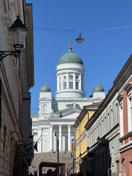 View of Helsinki Cathedral framed by old city buildings under a clear blue sky.