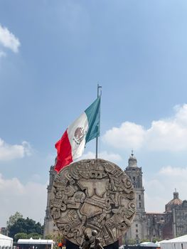 Iconic view of Mexico City's Zócalo featuring the Mexican flag, the Aztec calendar stone replica, and historic architecture.