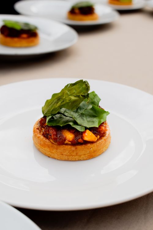 Free Appetizing mini tart topped with fresh green leaves and tomatoes on a white plate. Stock Photo