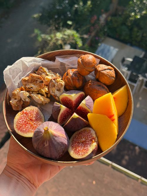 Free A wooden bowl with fresh figs, mango slices, and walnuts, held outdoors in daylight. Stock Photo