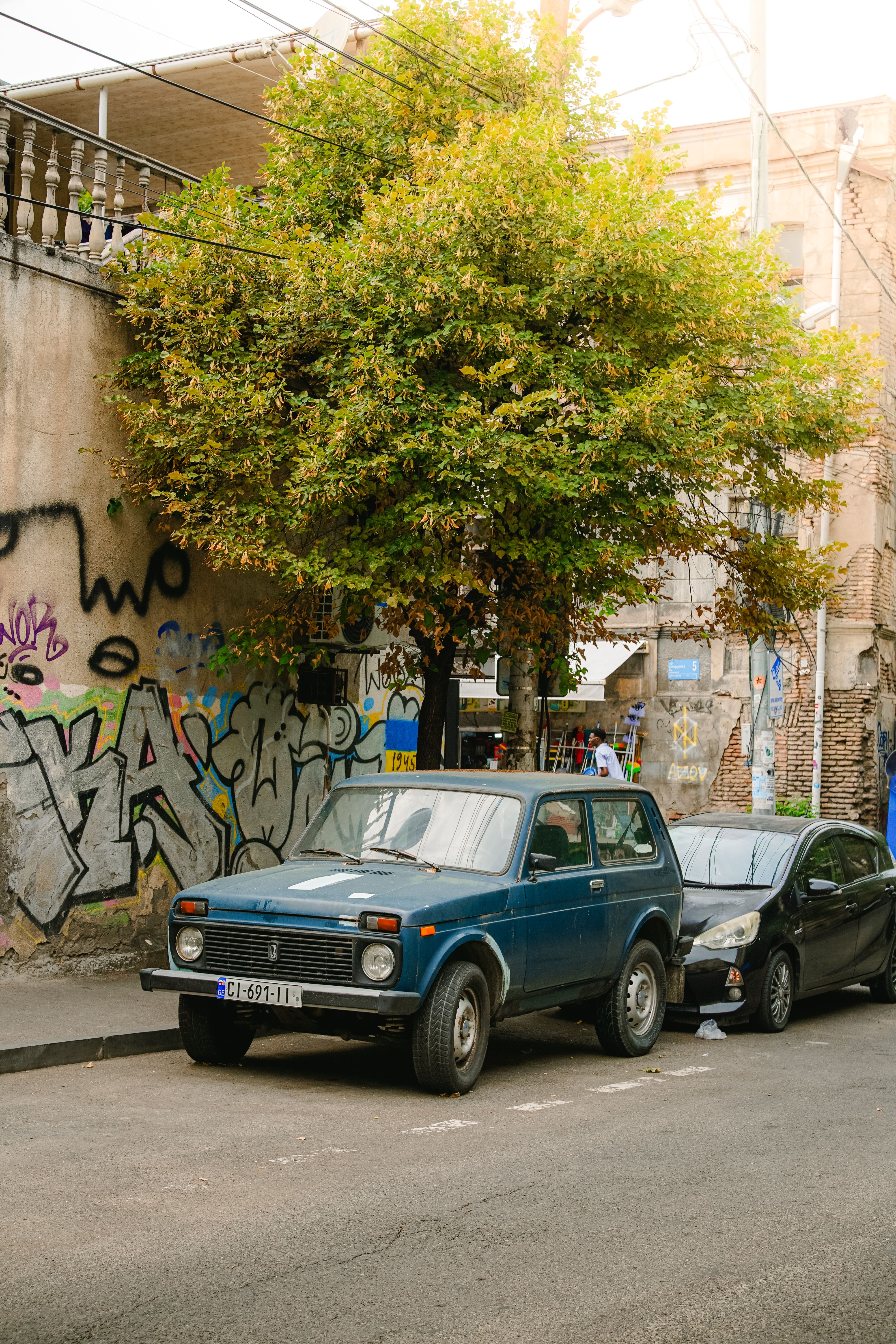 A blue Lada Niva parked on a graffiti-adorned street in Tbilisi, Georgia.