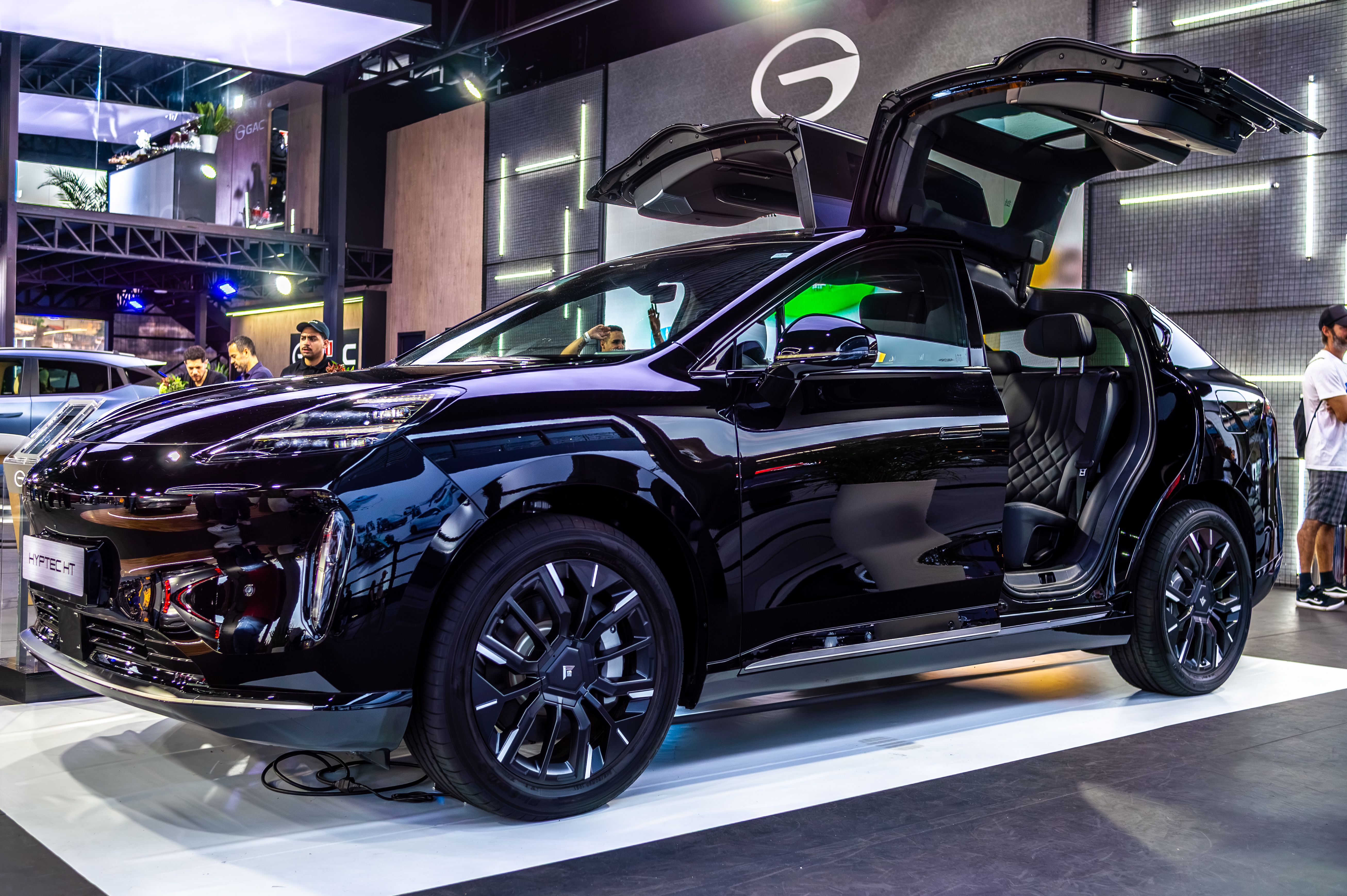 Black electric SUV with gullwing doors on display at an auto show.