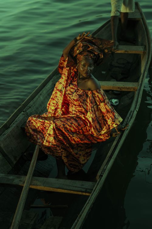 Free A woman in vibrant traditional dress poses elegantly on a boat during sunset. Stock Photo