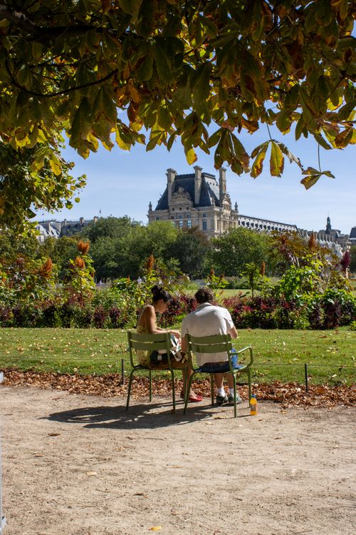 Free Couple relaxing in Paris's Tuileries Garden with Louvre in background. Stock Photo