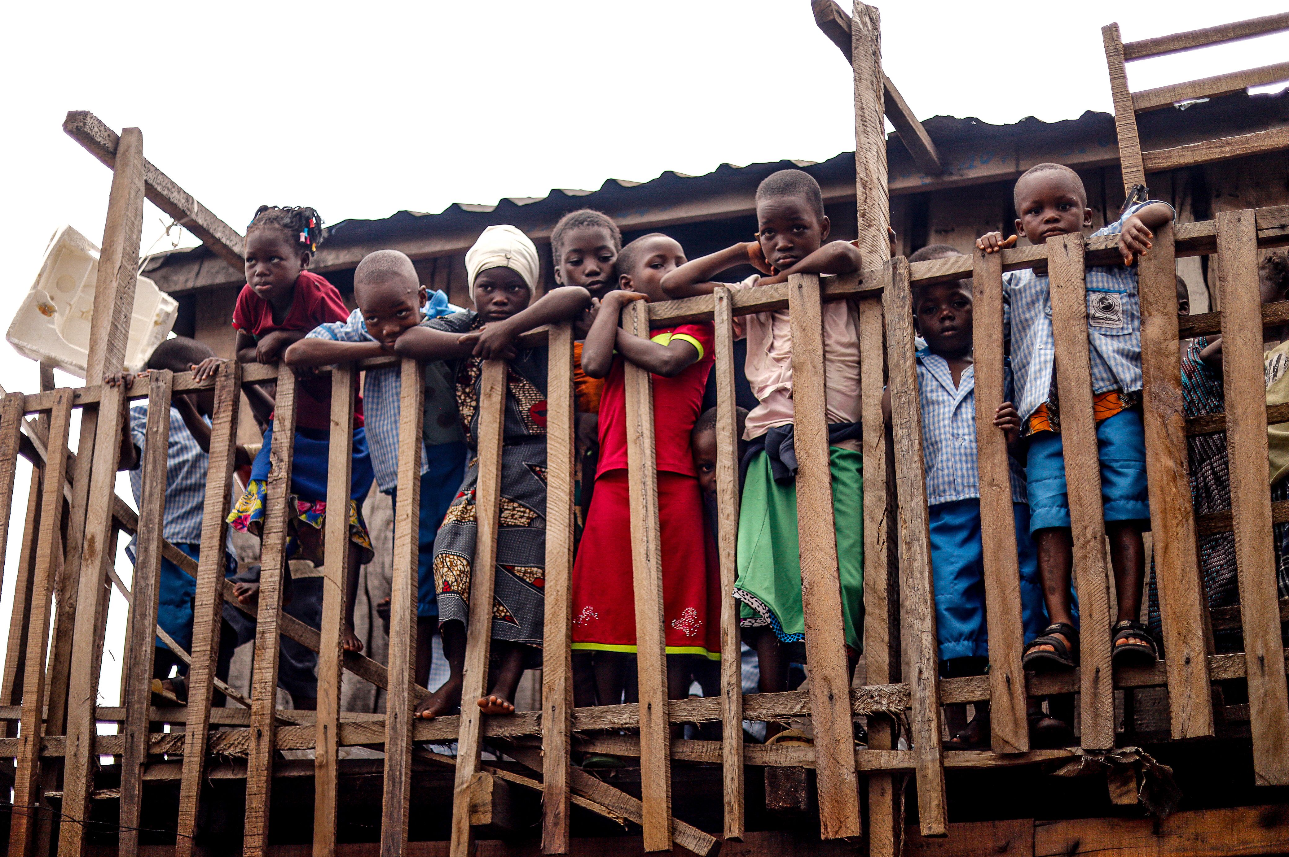 A group of curious children looking through a rustic wooden fence. Outdoors setting.