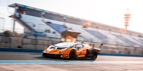Free Orange sports car racing on track with stadium background, motion blur effect. Stock Photo