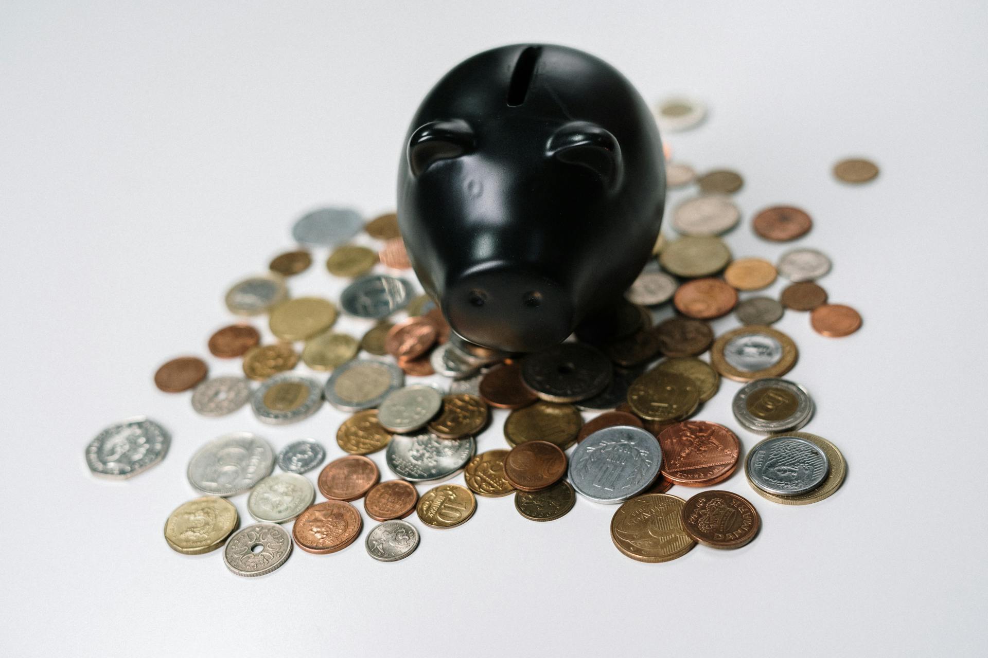 Black piggy bank surrounded by a variety of coins on a white surface, symbolizing savings and finance.