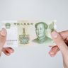 A close-up view of hands carefully holding a single one Chinese yuan banknote.