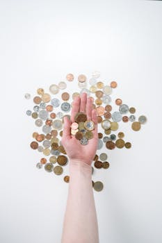 An open hand holds various coins on a white surface, symbolizing finance and currency exchange.