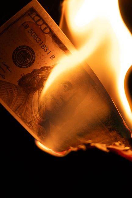 Close-up image of a burning $100 bill representing financial crisis or loss.