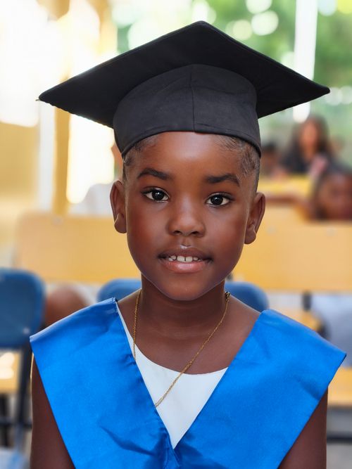 Free Adorable young child wearing a graduation cap and gown at a school ceremony, expressing pride and joy. Stock Photo