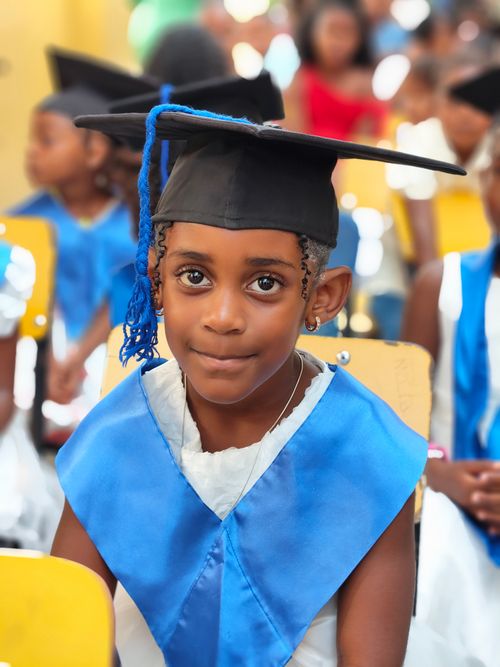 Free Smiling child in graduation cap and blue sash during a ceremony. Stock Photo