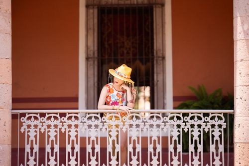 Free Stylish woman in floral dress and yellow hat on a decorative balcony outdoors. Stock Photo