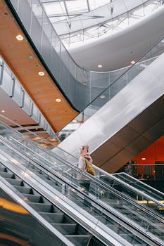 A woman wearing a face mask rides an escalator in a modern airport terminal, emphasizing travel safety.
