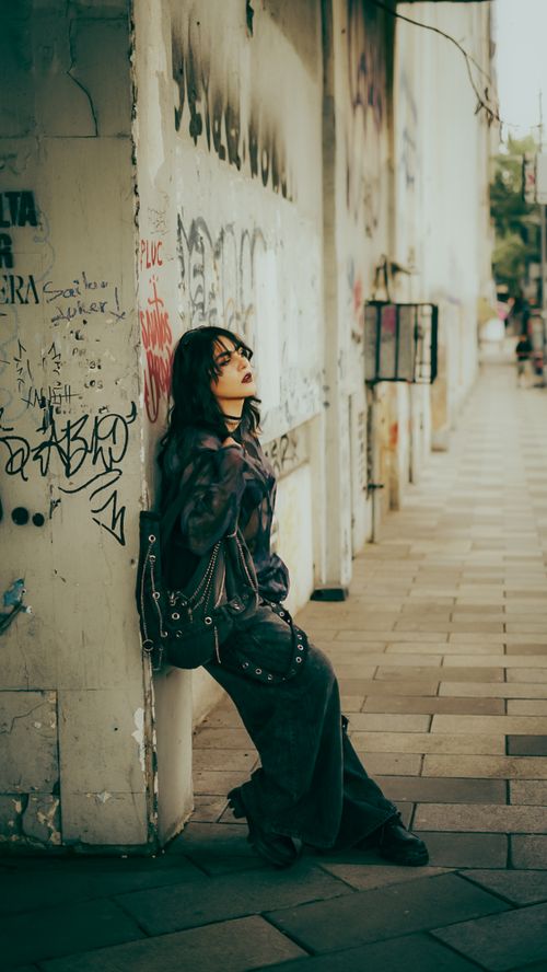Free Stylish woman in urban setting leaning on a graffiti-covered wall, conveying a cool and artistic vibe. Stock Photo