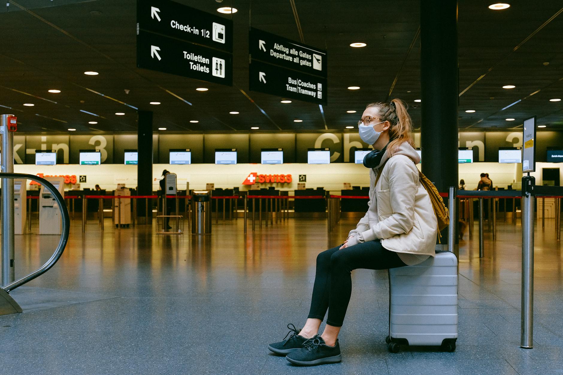 Woman sitting on luggage with mask on