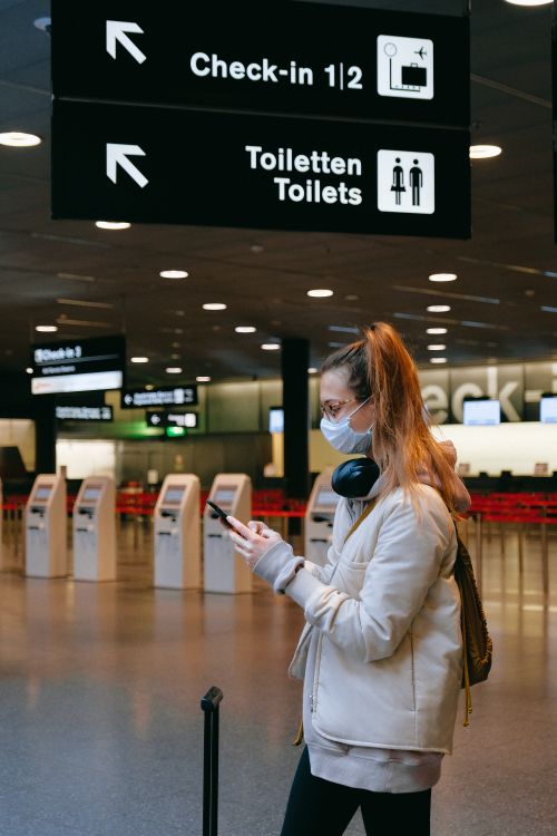 Free Woman wearing a mask, texting in airport terminal with signage in background. Stock Photo
