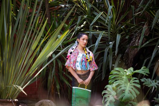 Young woman in traditional Mexican dress posing outdoors among lush greenery.