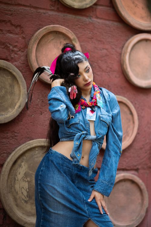 Free Fashionable woman in denim poses against an artistic wall with a colorful, cultural vibe. Stock Photo