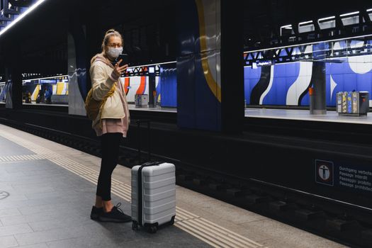 A traveler wearing a mask checks her phone on a subway platform during the pandemic.