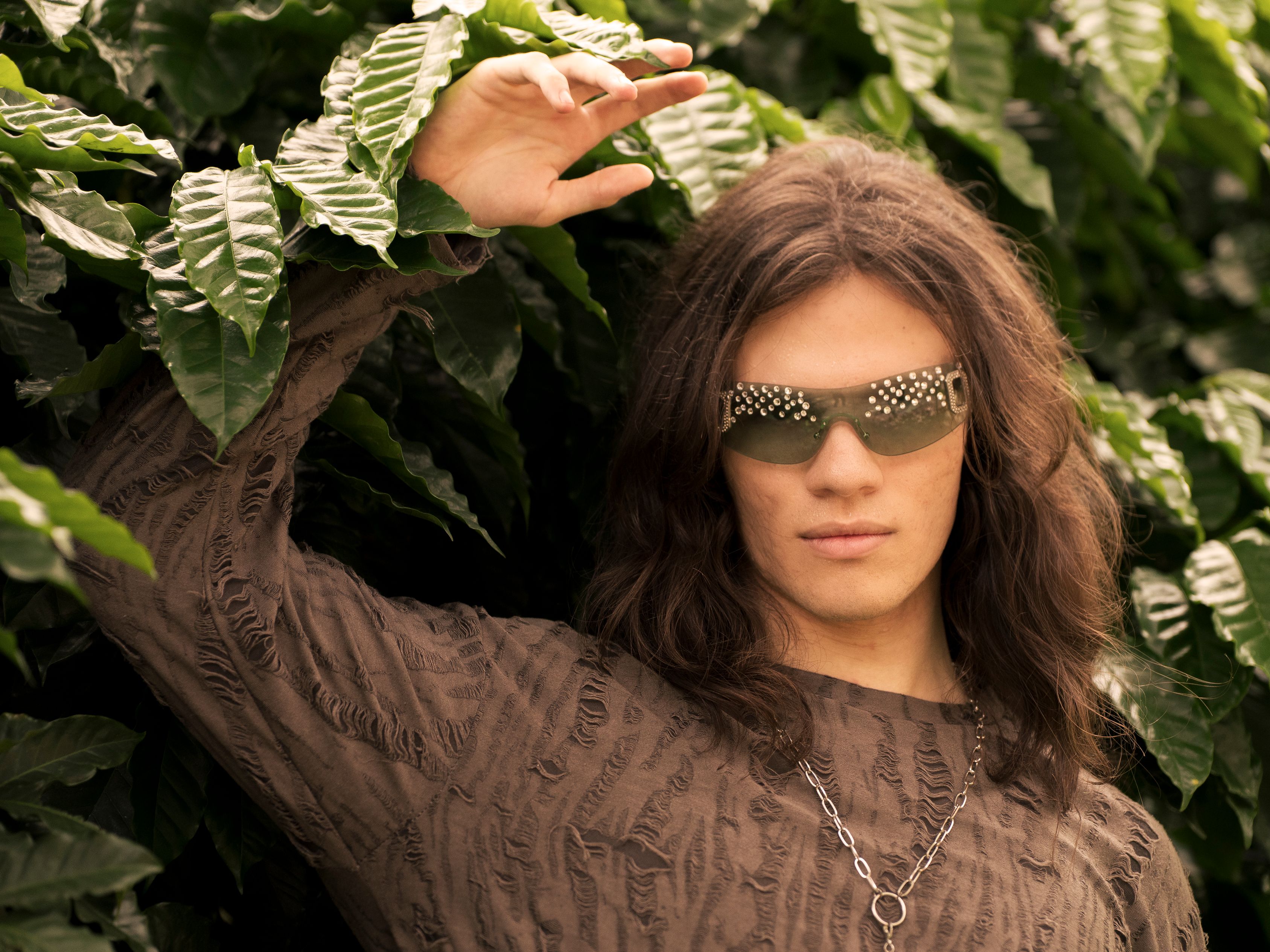 Stylish young adult wearing studded sunglasses standing among lush coffee plants in Costa Rica.