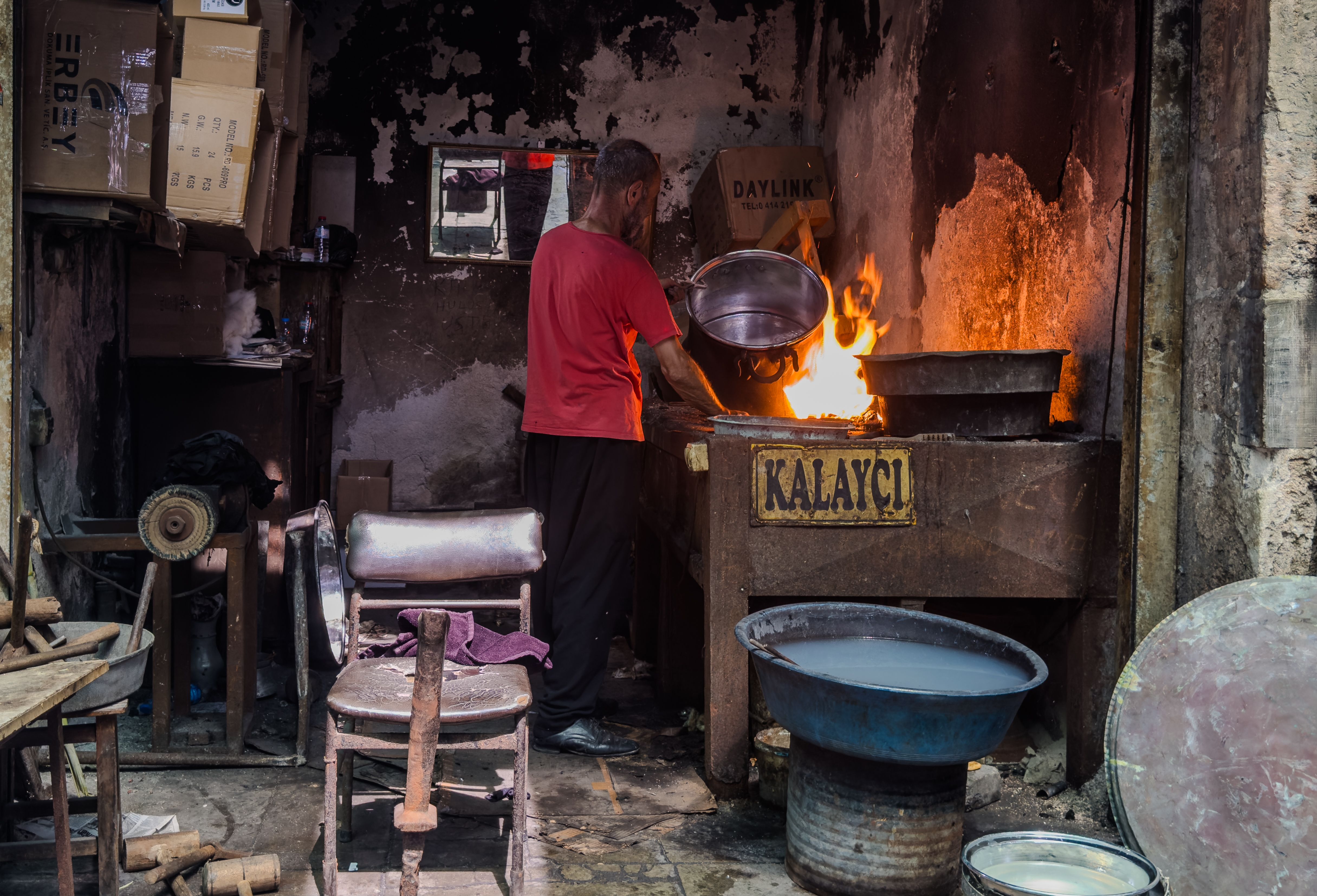 A craftsman in a dimly-lit workshop heats metal using a traditional fire stove.