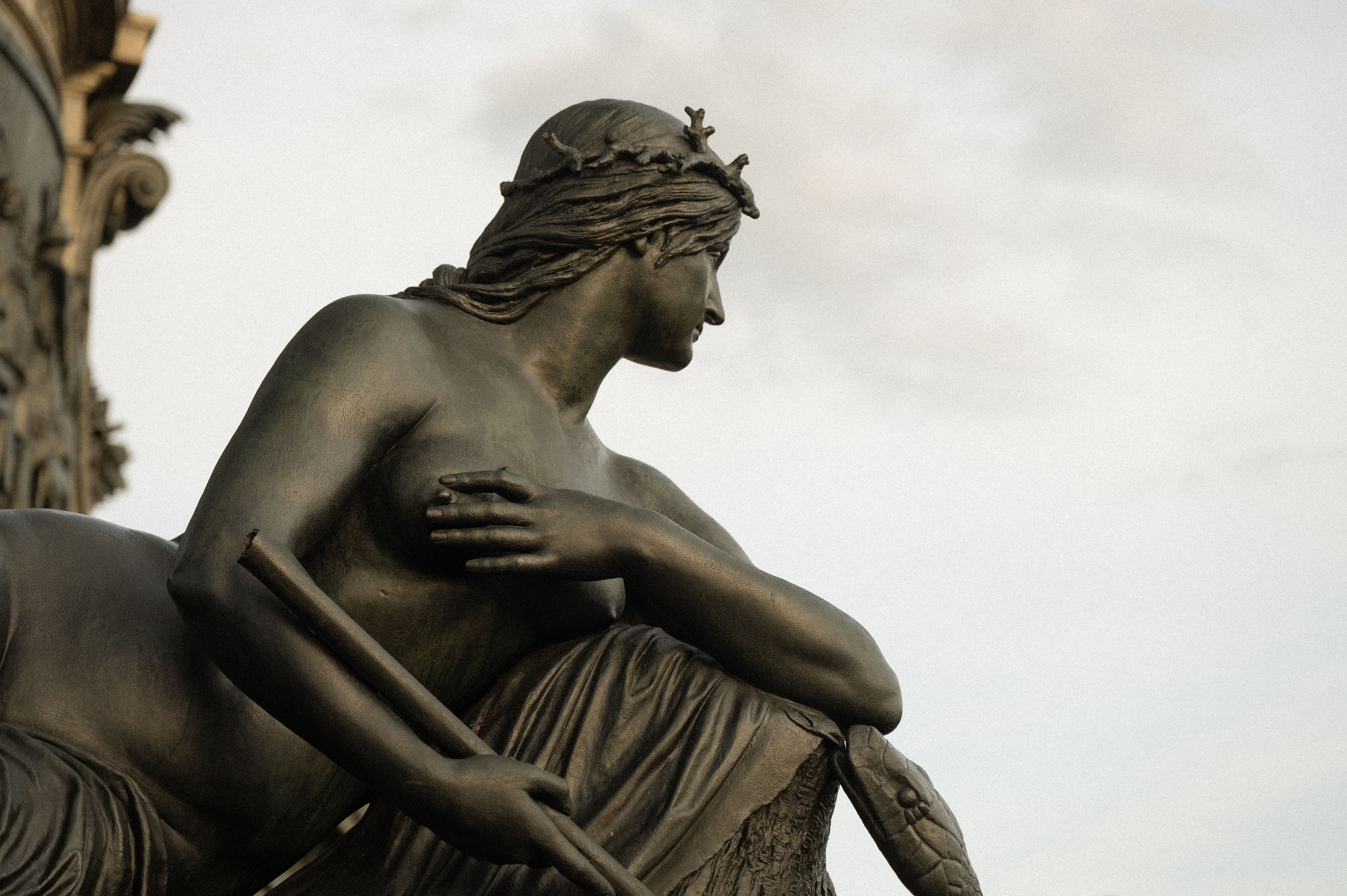 A close-up of a classical bronze statue showing intricate details set against a cloudy sky.