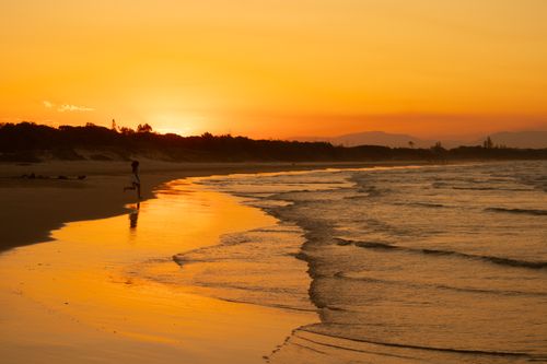 Free Golden sunset over a calm beach with a solitary runner, showcasing tranquility. Stock Photo