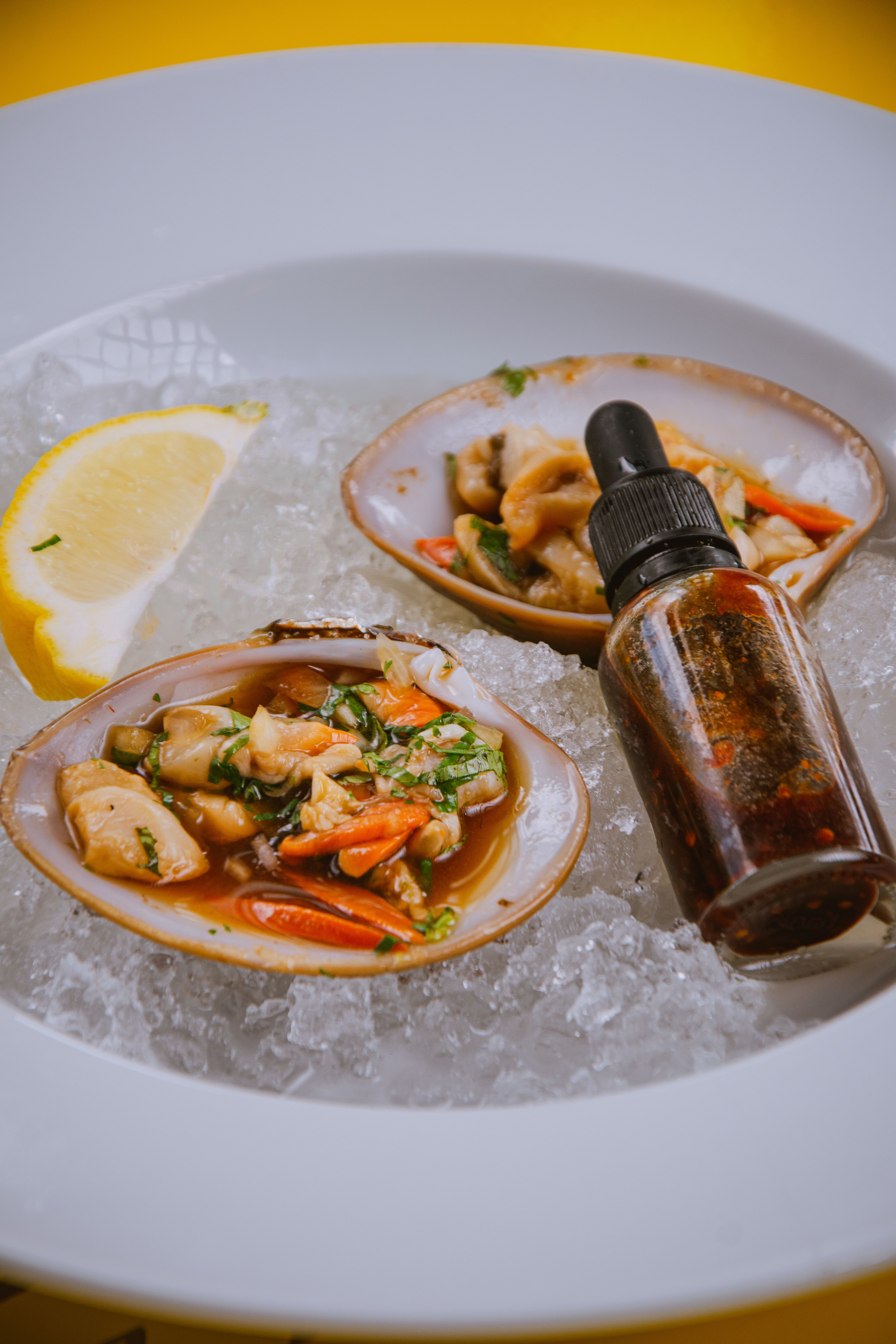 Fresh gourmet clams on ice with a lemon wedge and sauce dropper for seafood delicacy.