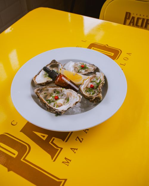 Free Plate of fresh oysters with lemon wedge and sauce on a yellow table. Stock Photo