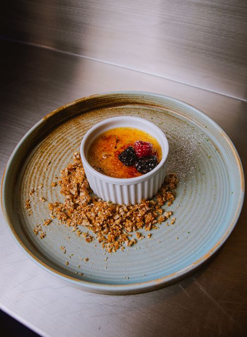 Free Delicious crème brûlée topped with fresh berries and crunchy granola on a rustic plate. Stock Photo