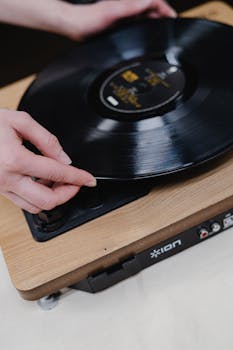 Close-up of hands placing a vinyl record on a vintage turntable, evoking a nostalgic music experience.