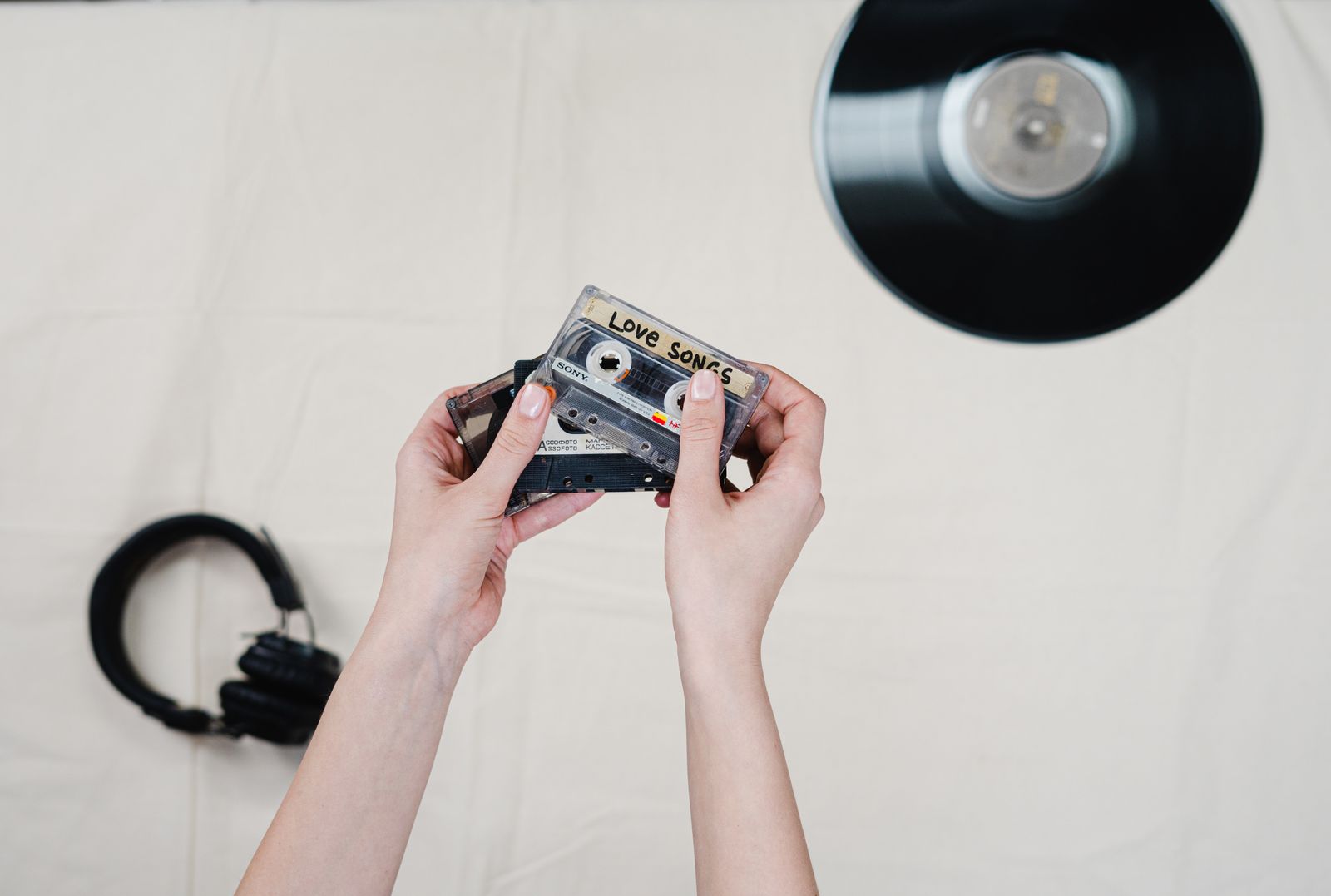 Hands holding a cassette labelled Love Songs beside headphones and a vinyl record