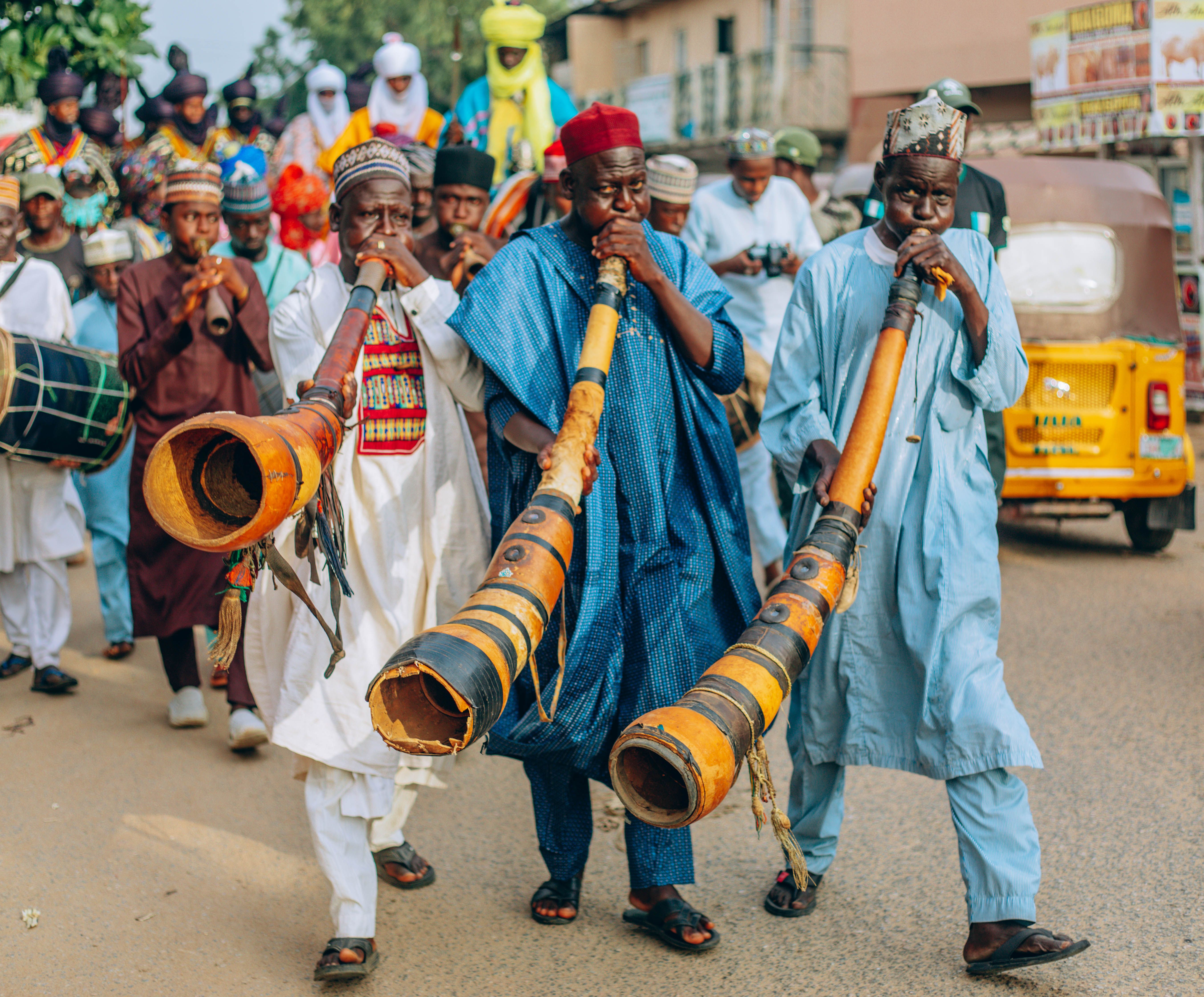 Nigerian musicians in vibrant attire perform in a lively street parade with traditional instruments.