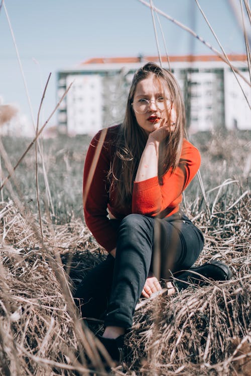 Woman in Red Long Sleeve Shirt and Black Pants Sitting on Brown Grass